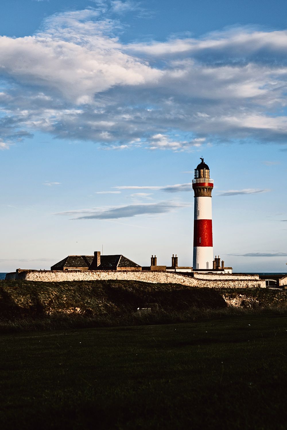 Red and white lighthouse under a tall blue sky with clouds, Aberdeenshire coast