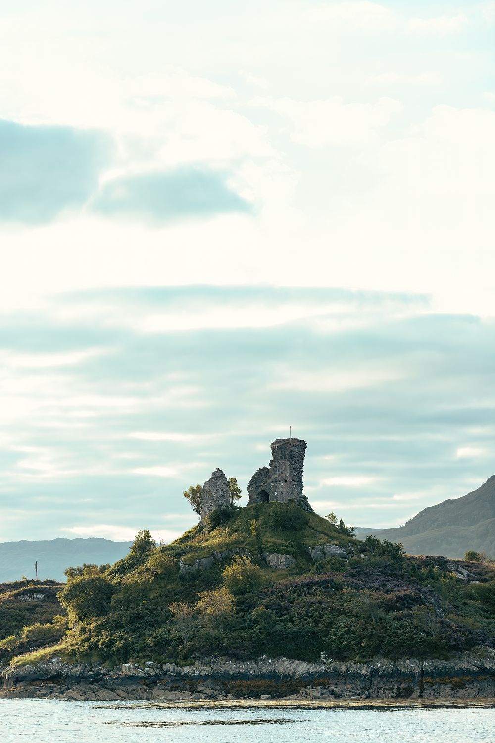 A ruined castle on a rocky headland under a big pale sky, Scottish Highlands