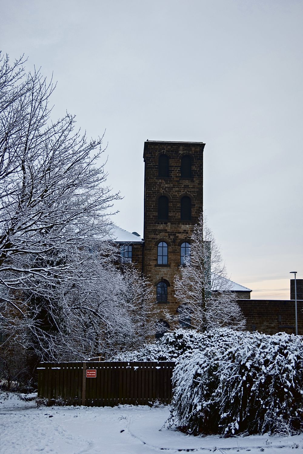 An old stone mill tower beside snow-laden trees under a pale winter sky