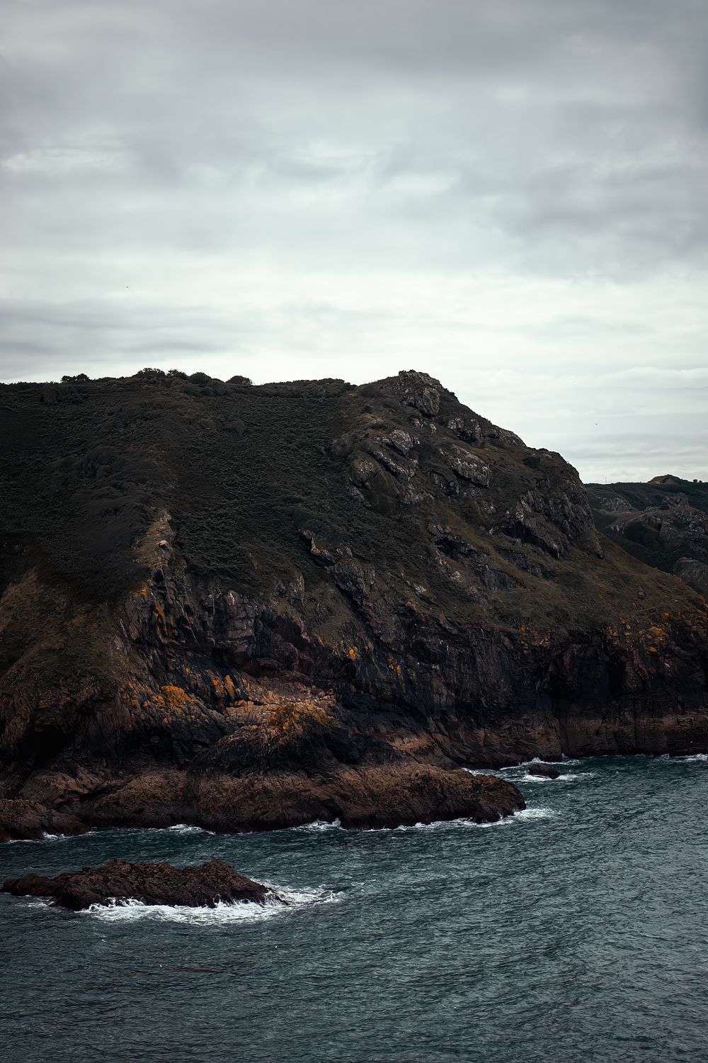A dark headland above slate-grey sea under a cloudy sky, Jersey