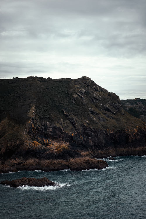 A dark headland above slate-grey sea under a cloudy sky, Jersey