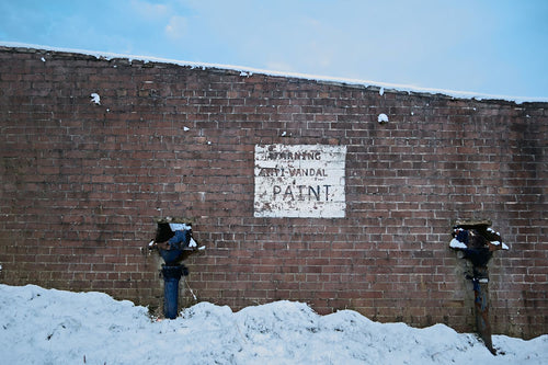 A hand-painted 'warning, anti-vandal paint' sign on an old brick wall above fresh snow