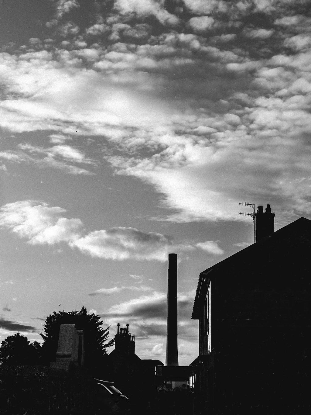 Rooftops and a tall chimney silhouetted under a mackerel sky, Aberdeenshire, in black and white