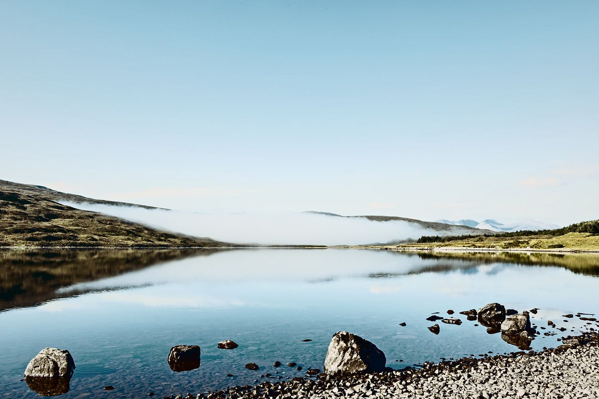 Rocks in a perfectly still loch reflecting the hills and a clear blue sky, Scottish Highlands