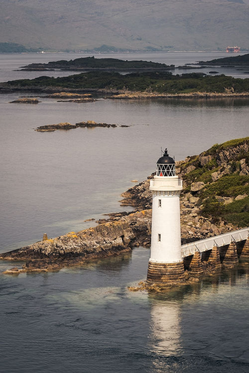 Kyleakin lighthouse and walkway reflected in calm water, with islands beyond