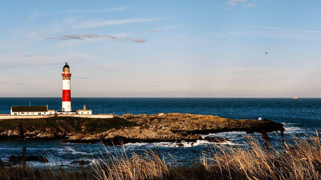 Red and white lighthouse and keepers' cottages above the North Sea, with golden grasses in front, Aberdeenshire