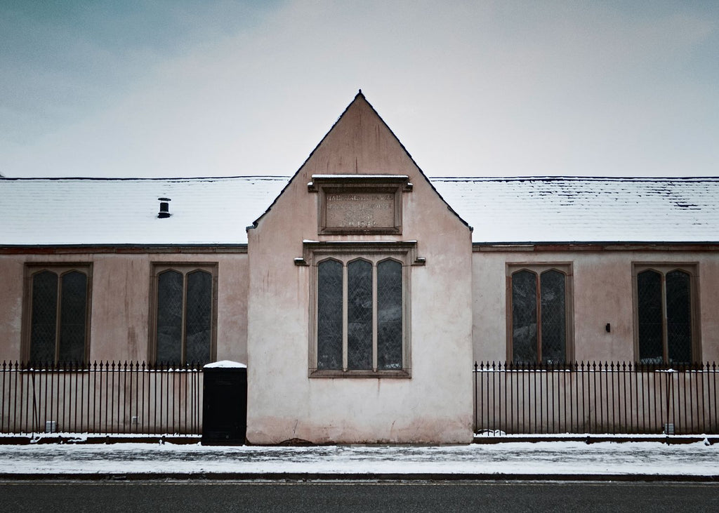 The symmetrical gable of an old chapel hall with iron railings and a dusting of snow