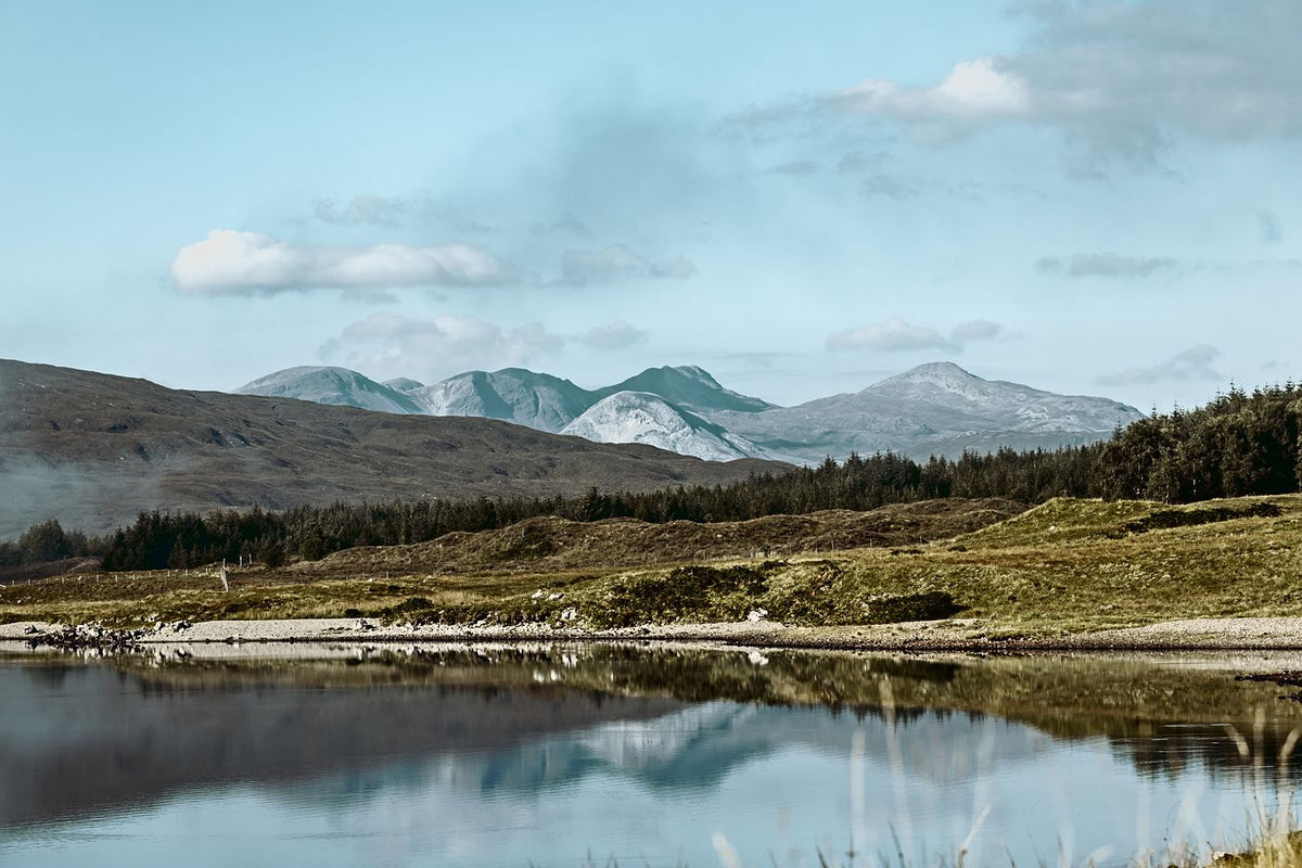 Snow-dusted mountains and green hills reflected in a still loch under a blue sky, Scottish Highlands