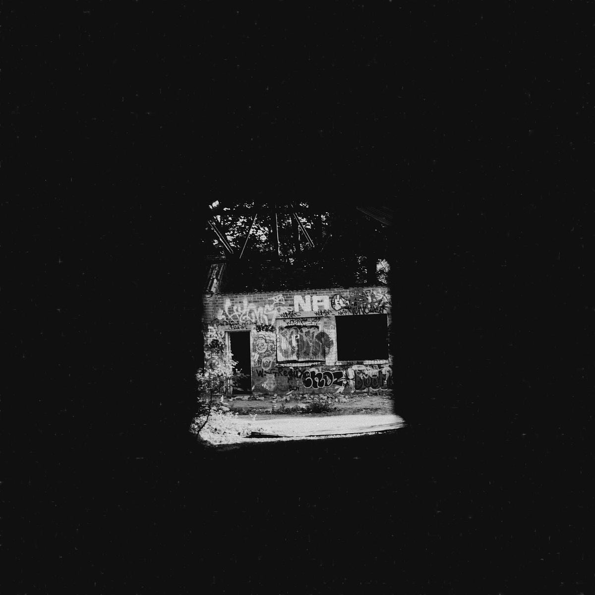Black and white photograph of a graffitied ruin seen through a dark opening